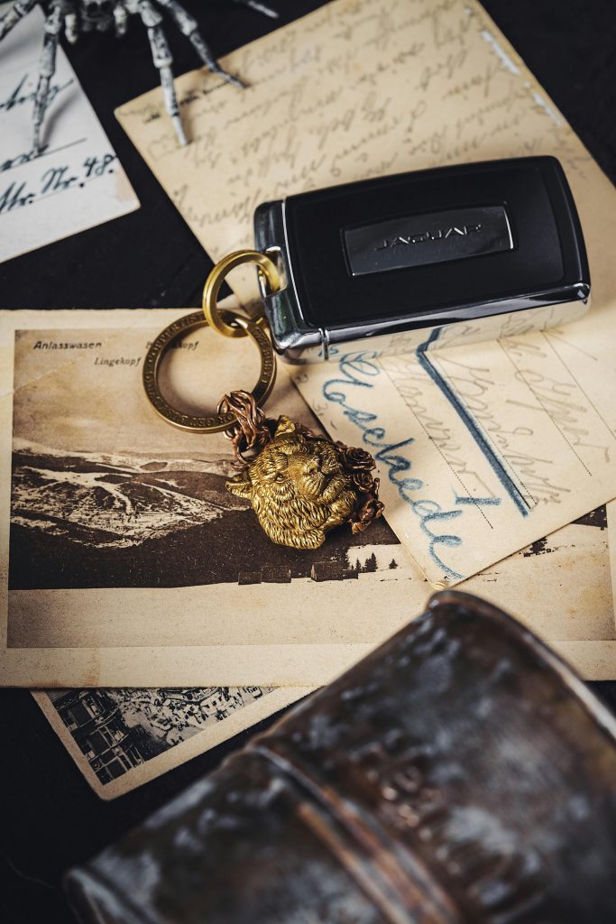 A modern car key resting on vintage postcards with a lion-head keychain.